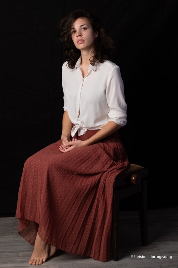 Studio portrait in a white shirt and terracotta skirt against a dark backdrop