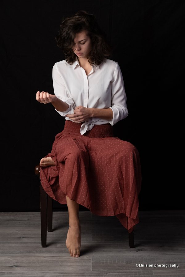 Studio portrait in a white shirt and terracotta skirt against a dark backdrop