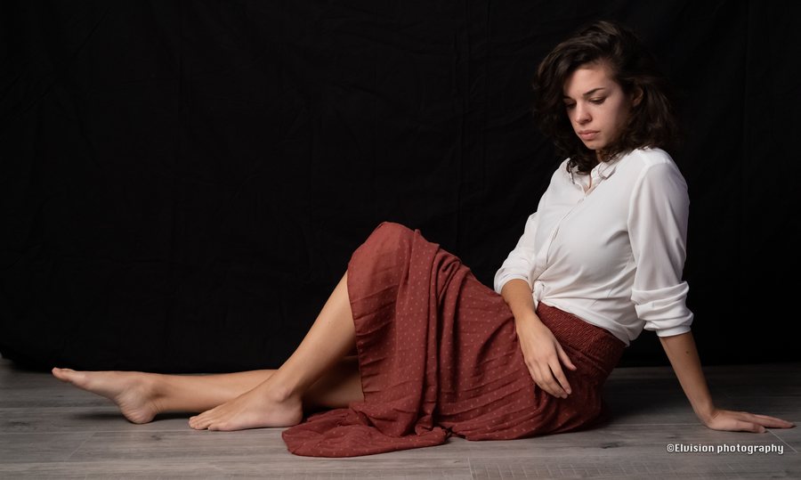 Studio portrait in a white shirt and terracotta skirt against a dark backdrop