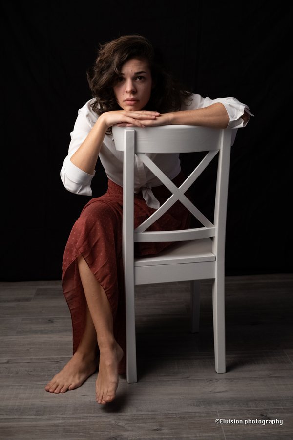 Studio portrait in a white shirt and terracotta skirt against a dark backdrop