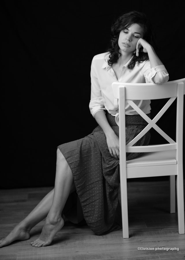Studio portrait in a white shirt and ash-grey skirt against a dark backdrop