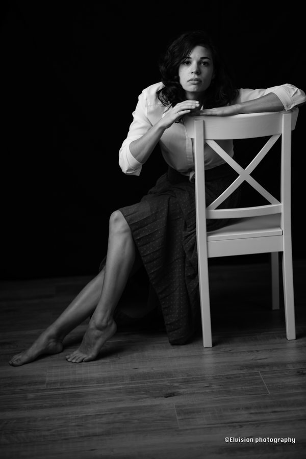 Studio portrait in a white shirt and ash-grey skirt against a dark backdrop