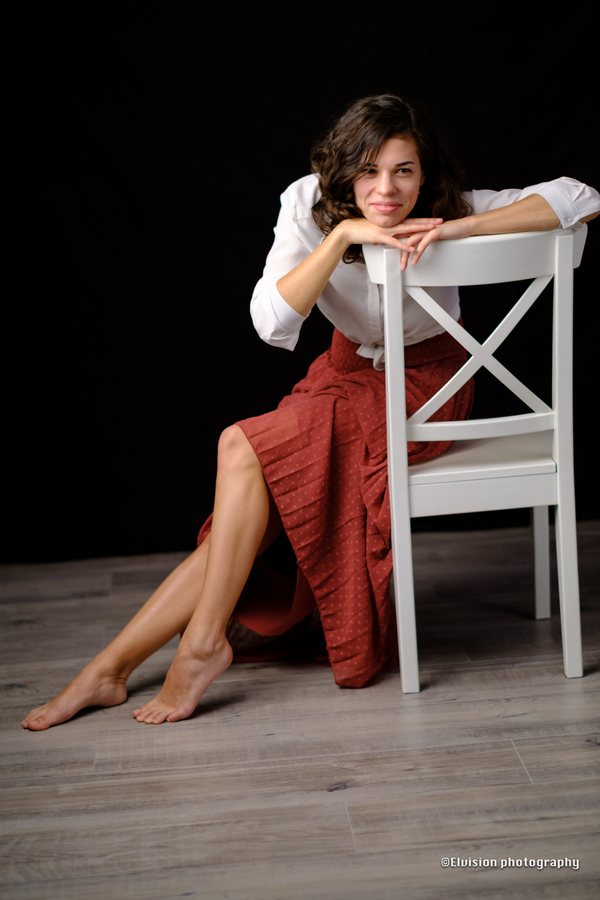Studio portrait in a white shirt and terracotta skirt against a dark backdrop