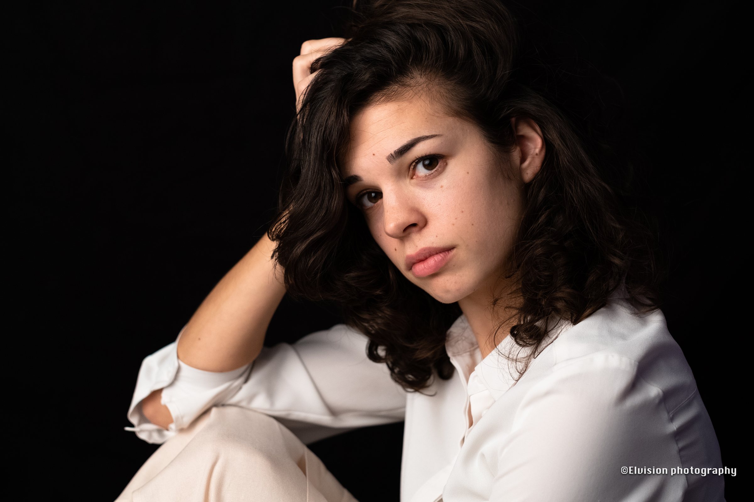 Studio portrait of a woman in a white shirt lit against a dark backdrop